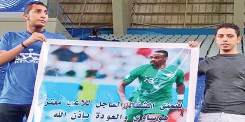  لقطة لمشجعي الهلال يحملان لافتة تتمنى الشفاء لهوساوي